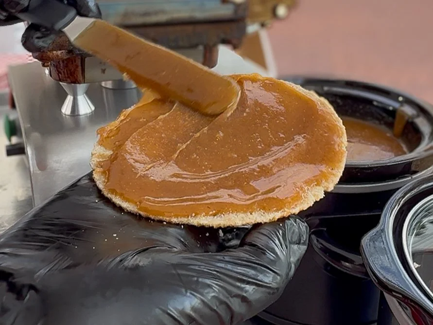 Warm caramel being spread on a freshly baked Dutch stroopwafel during a live stroopwafel baking experience