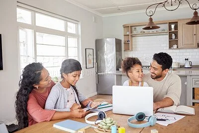 A family of four sitting at a kitchen table using a laptop, with books and electronic devices in a bright, modern kitchen.