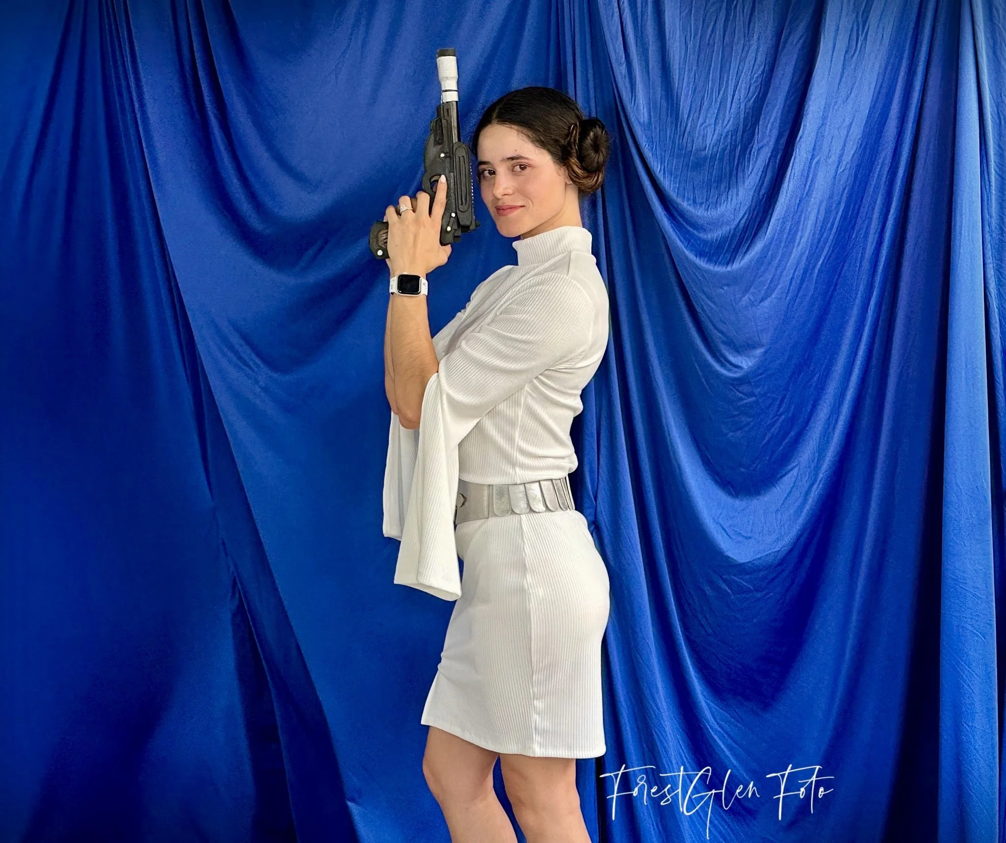 Person in sci-fi character costume holding a futuristic blaster, standing against a blue fabric backdrop.