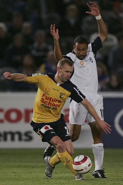 Two soccer players competing for the ball on the field during a match, with one in a yellow jersey and the other in a white jersey.