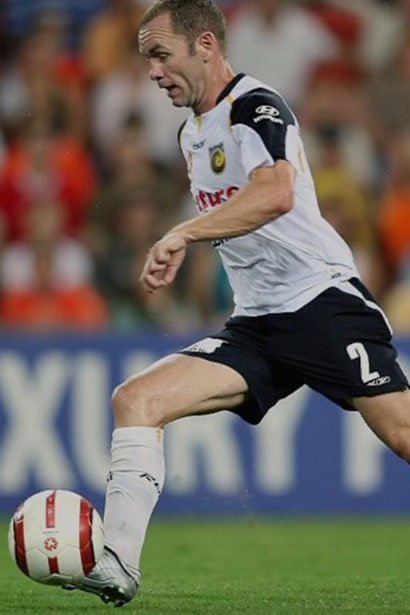 A soccer player in a white and black uniform kicking a red and white ball on the field during a match.