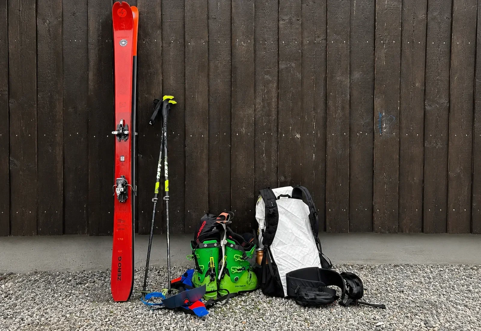 Touring skis, poles, ski boots and a backpack against a dark wooden wall