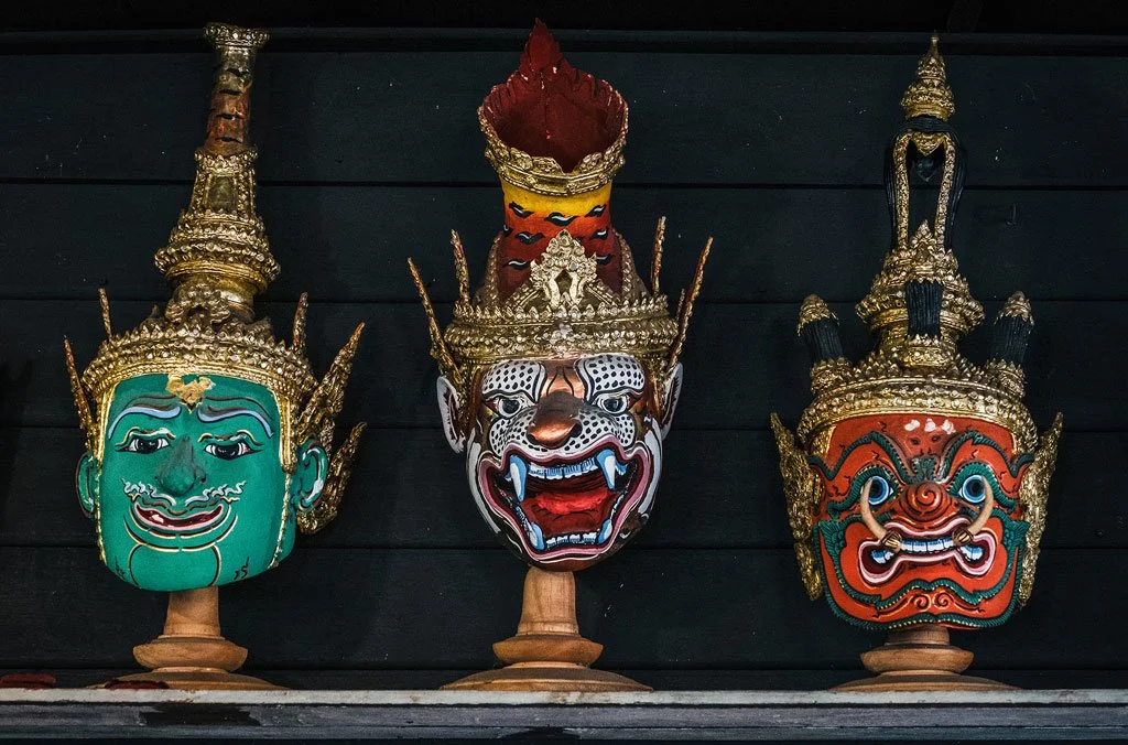 Three traditional Thai masks with elaborate headdresses displayed against a dark background.