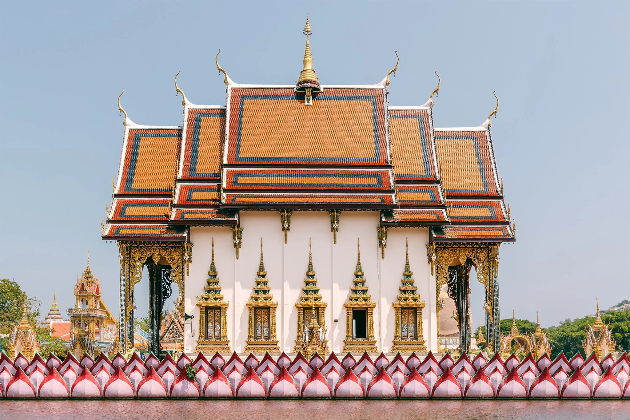 Traditional ornate Thai temple with multi-tiered roof and intricate gold detailing, against a clear blue sky.