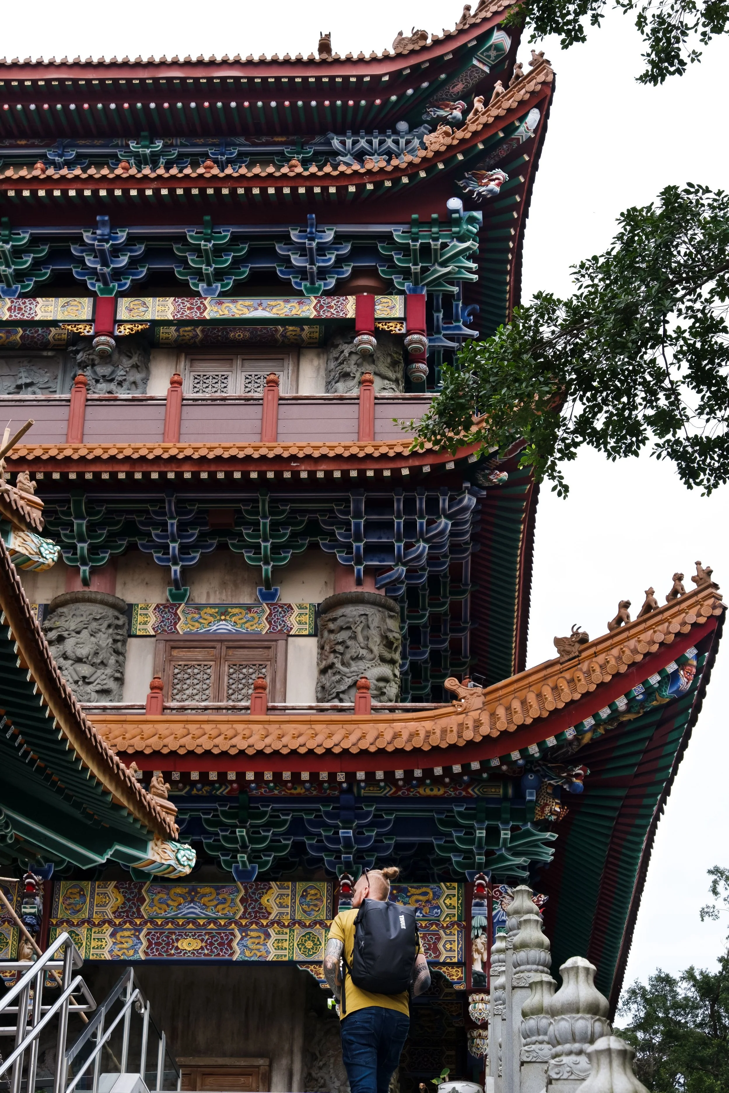 A person with a yellow shirt and backpack entering a traditional Asian temple with intricate, colorful architectural details.