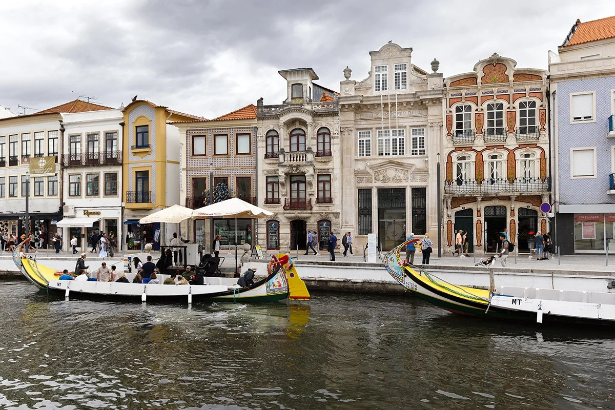 Colorful boats docked by a canal with historic buildings and pedestrians in a cityscape