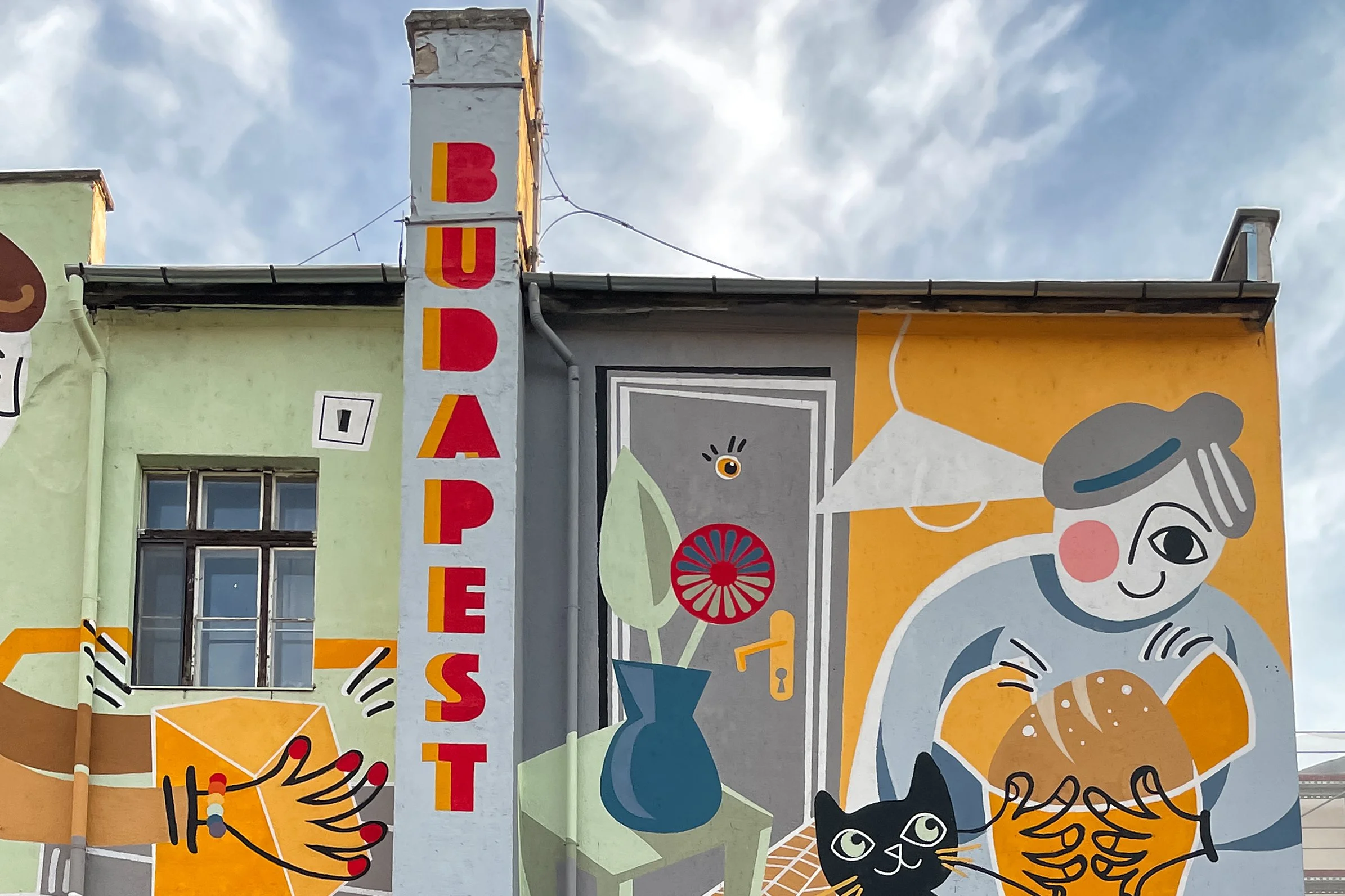 Colorful mural on the side of a building featuring abstract and cartoon-style illustrations, including a smiling person with gray hair, a black cat, a blue water pitcher, and the word 'DRAFT' written vertically in bold letters.