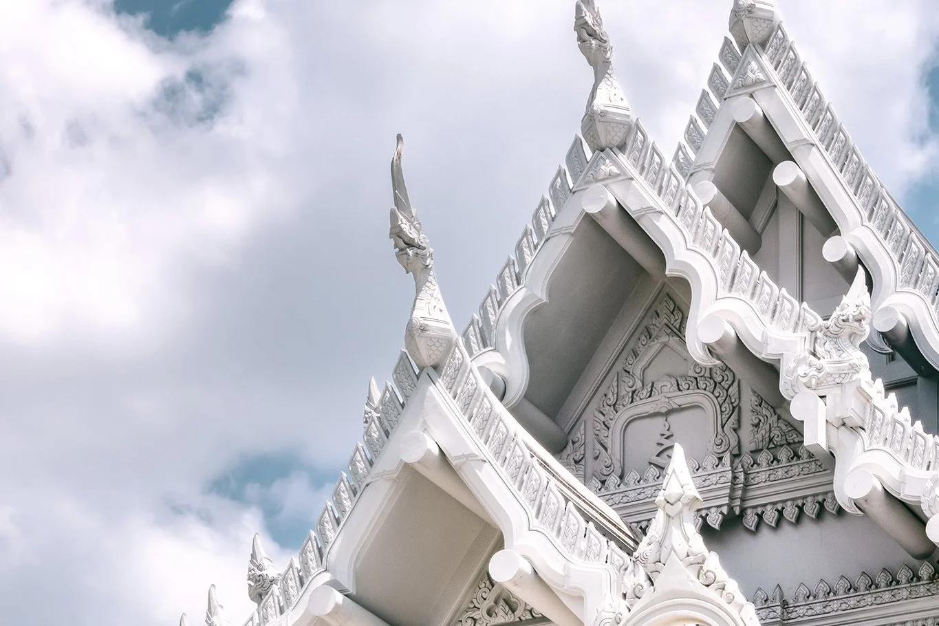 Close-up of a white ornate temple roof with decorative spires and intricate carvings against a cloudy sky.
