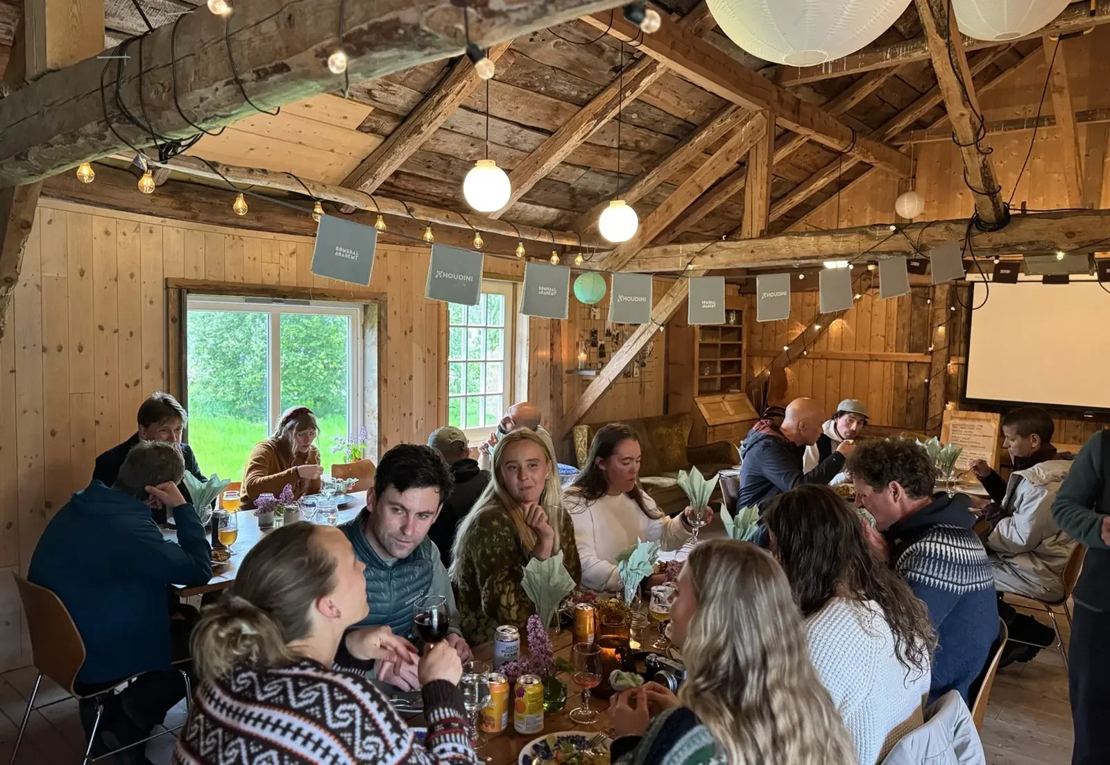 People sharing a meal at long tables inside a wooden barn
