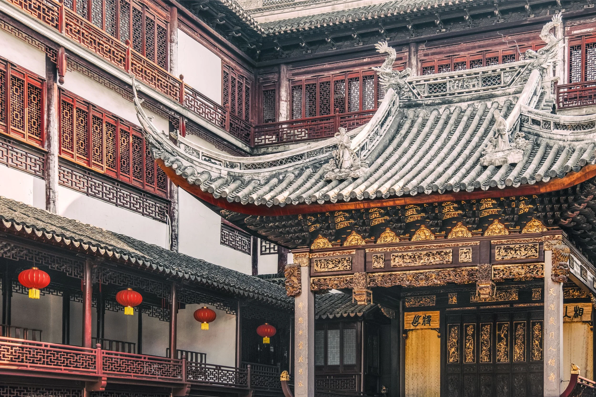 Close-up of traditional Chinese temple architecture with intricate woodwork, dragon sculptures on the roof, and red lanterns hanging outside.