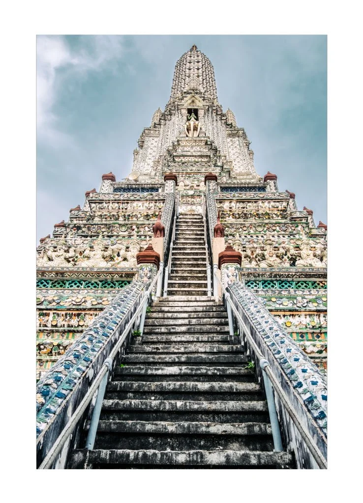 A tall, ornate temple with decorative tiles and sculptures, featuring stairs leading up to the entrance, under a partly cloudy sky.