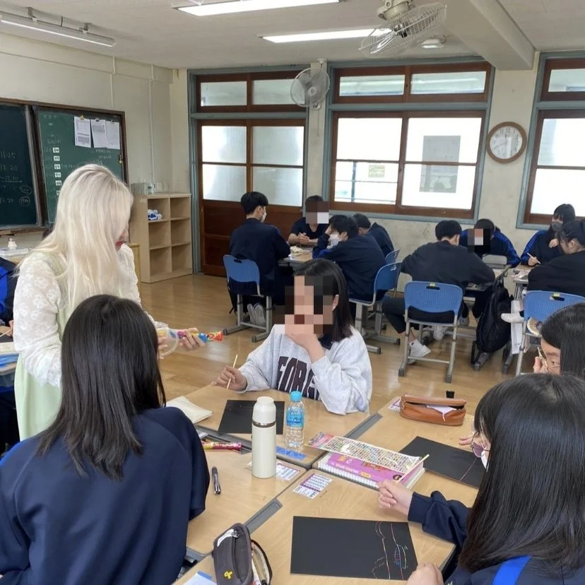 Une classe avec des élèves en uniforme assis à des tables, une femme blonde distrayante distribuant des bonbons à un groupe d'élèves dont le visage est pixélisé.