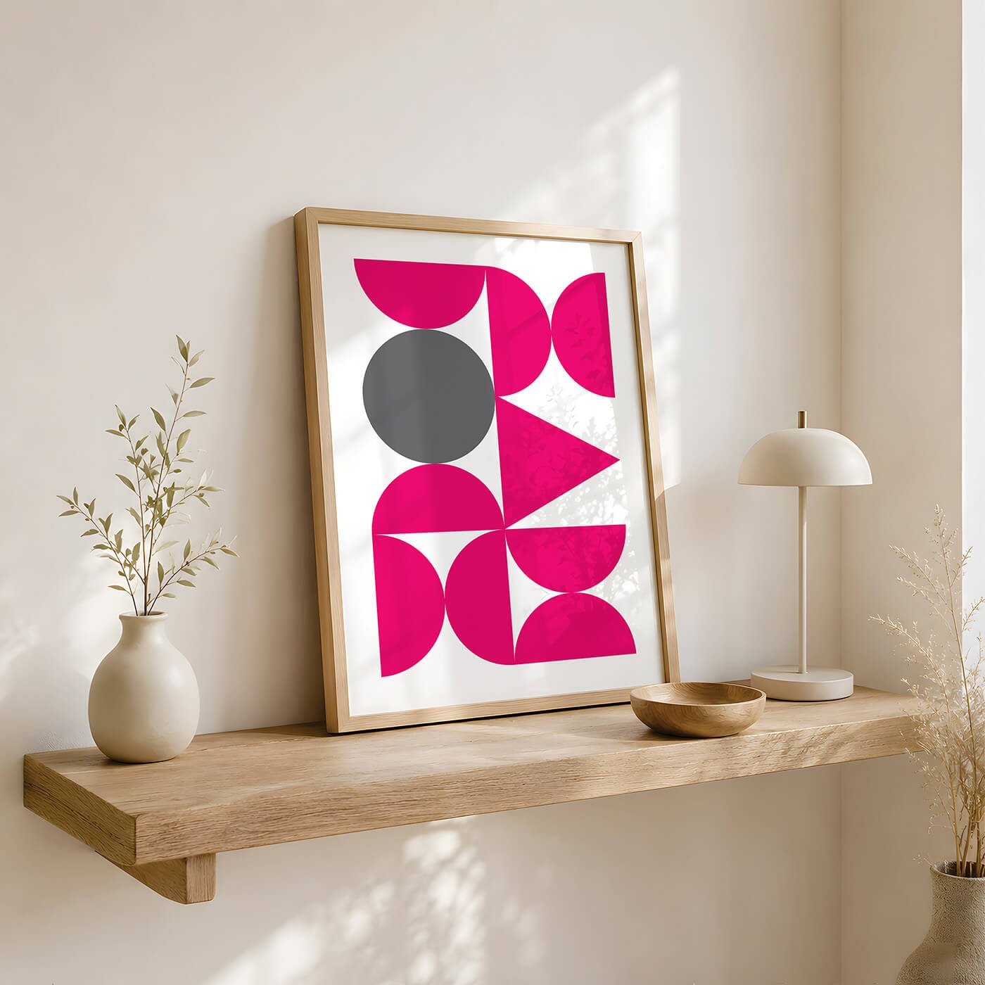 Pink Abstract Forms Print in a wooden frame styled on a contemporary sideboard with decorative books, a modern bowl and a plant next to a window.