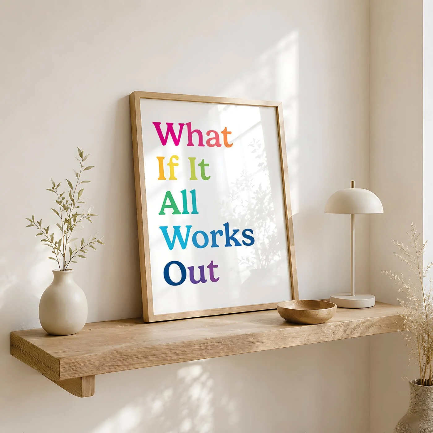 A mid century rainbow typography print reading What If It All Works Out, displayed in a wooden frame on a natural timber floating shelf with a neutral ceramic vase and a small wooden bowl
