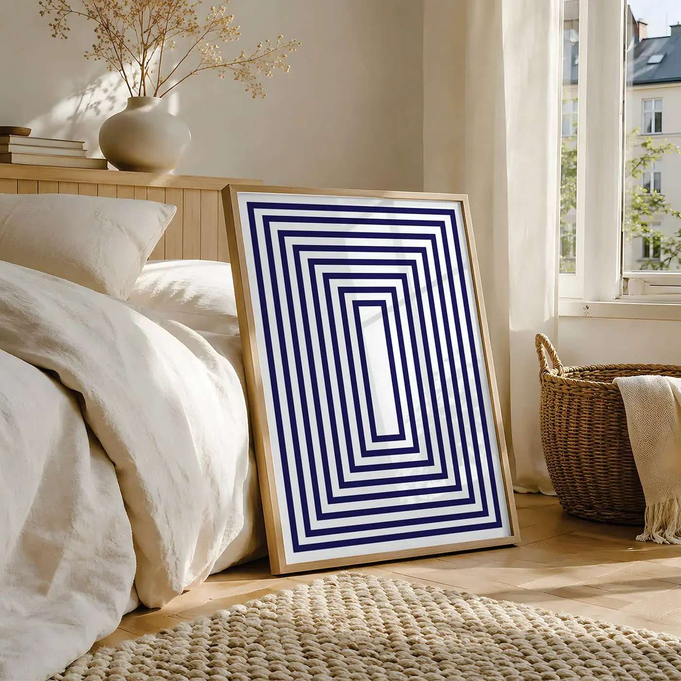 A bedroom with a bed that has striped bed linens, a wooden nightstand with a bear-themed mug, and a framed poster with orange circles and the word "Glow" on a white wall.