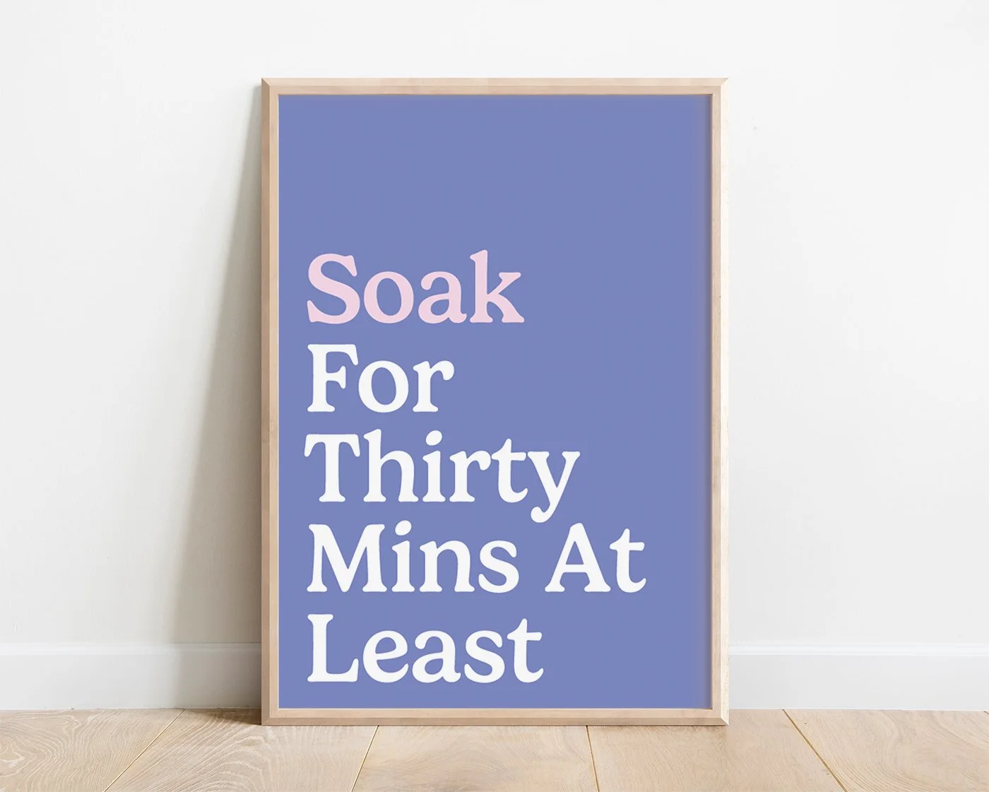 A contemporary pastel bathroom typography print featuring soft blue and white text reading Soak For Thirty Mins At Least, in a wooden frame on a bright white bathroom wall.
