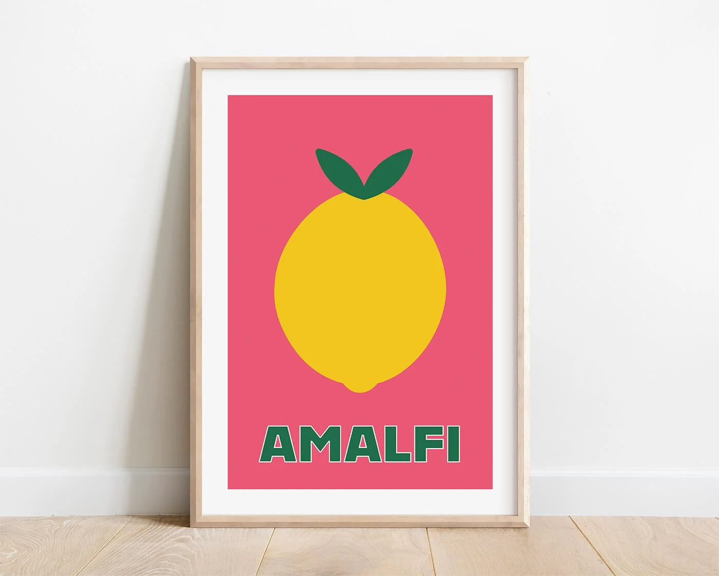 A colourful summer fruit poster featuring a yellow Amalfi lemon on a bright pink background, showcase-mounted in a simple wood frame on a modern white interior wall