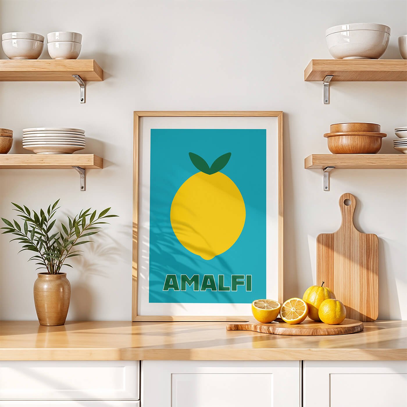 A framed blue Amalfi lemon art print sitting on a clean kitchen worktop in a bright, modern white kitchen space