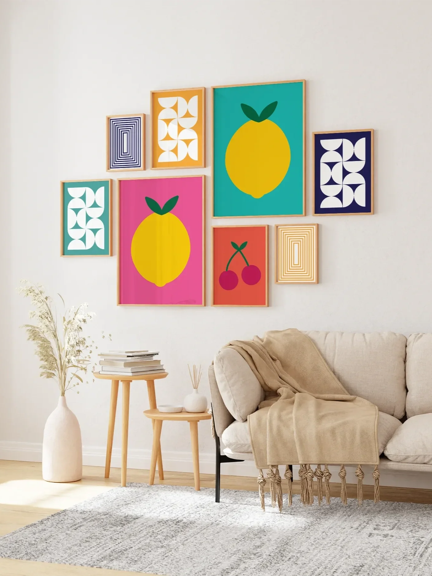 Living room with a beige sofa, a white vase with pampas grass, a small stack of books, a wooden side table, and a gallery wall of colorful geometric and fruit artwork.