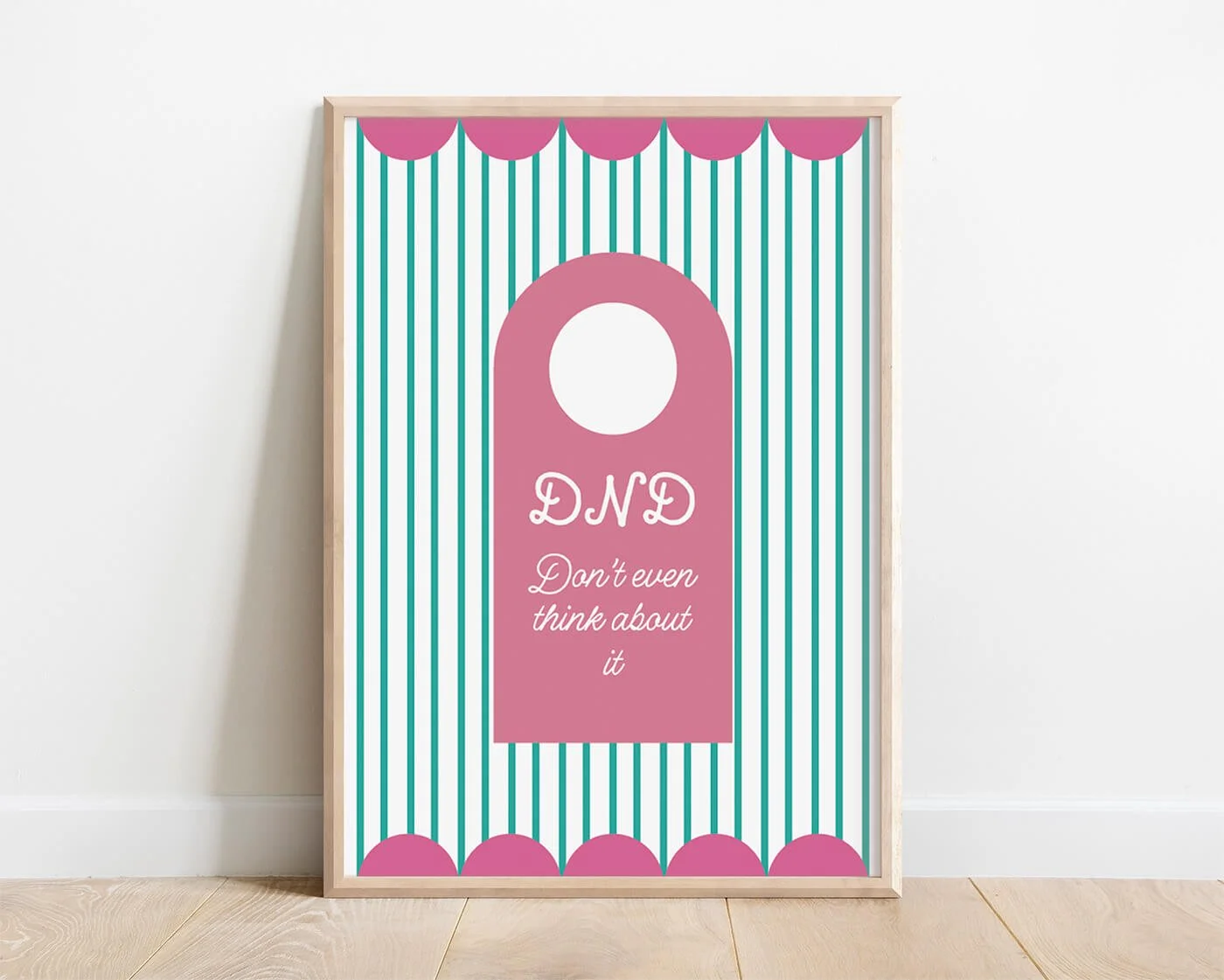 Pink Do Not Disturb Print shown in a natural wooden frame leaning against a white interior wall.