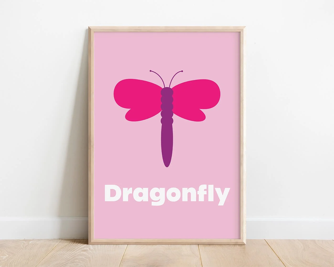 Dragonfly Learning Print in a modern oak wooden frame displayed on a white interior wall. Contemporary dragonfly illustration on a colourful pink background with the word "Dragonfly" beneath.