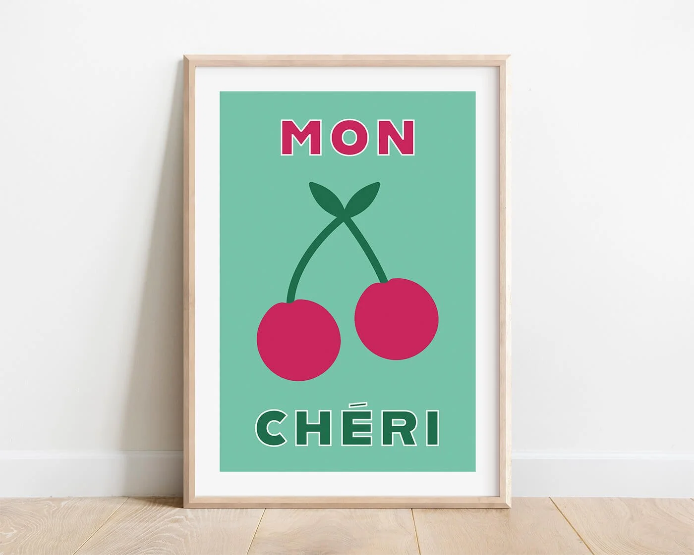 Green Mon Cheri typography art print in a natural wooden frame hanging on a white interior wall by Amatus