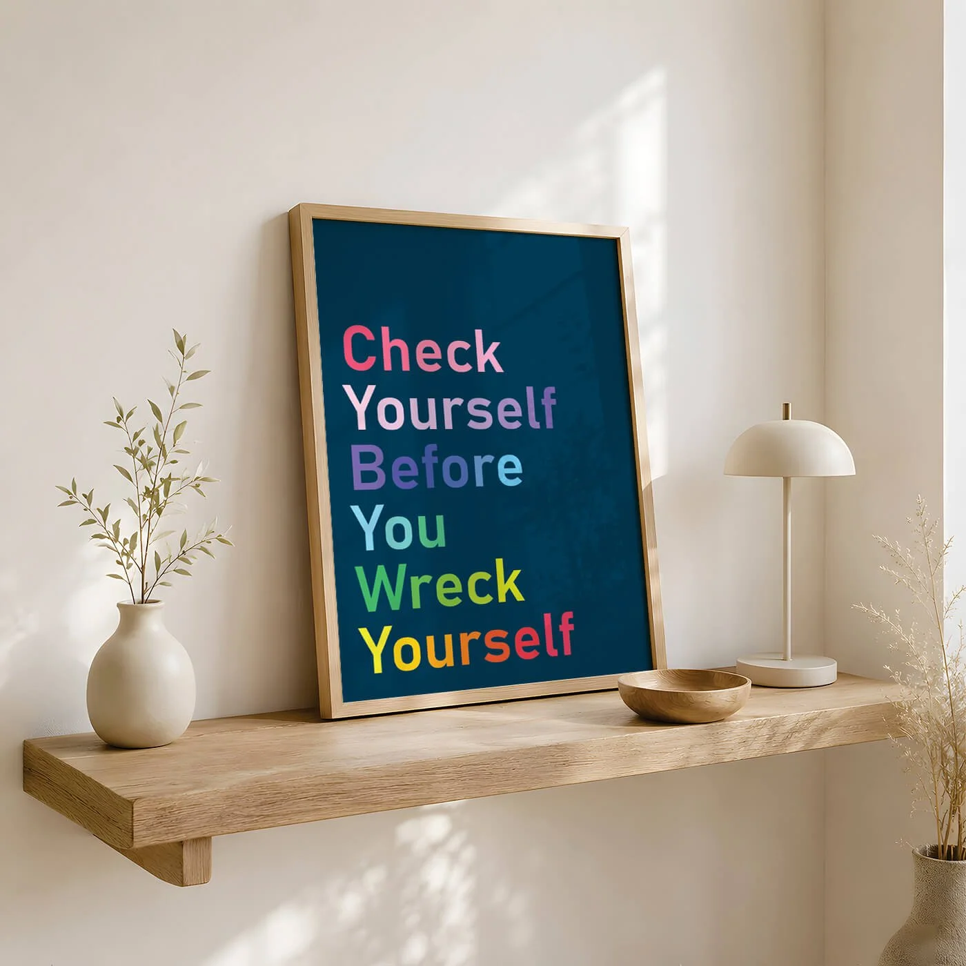 Rainbow Check Yourself print in a wooden frame on a wooden shelf in a neutral living room