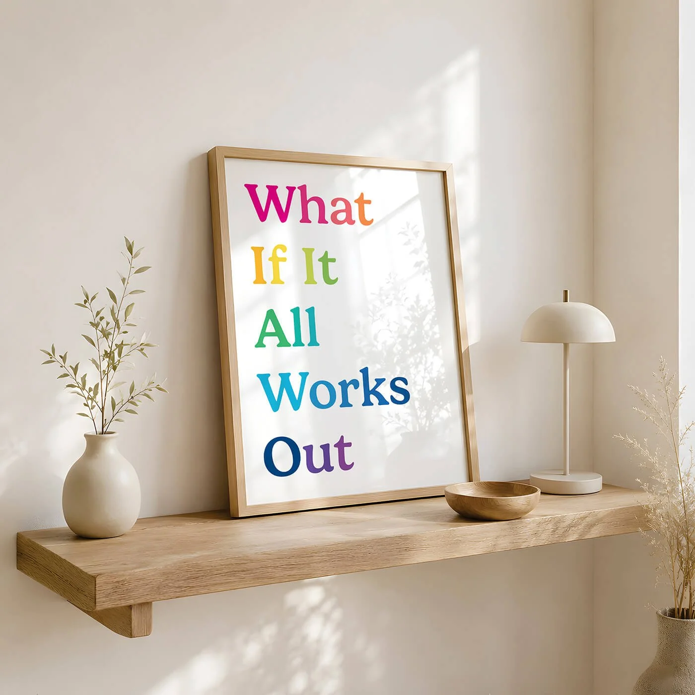 A mid century rainbow typography print reading What If It All Works Out, displayed in a wooden frame on a natural timber floating shelf with a neutral ceramic vase and a small wooden bowl