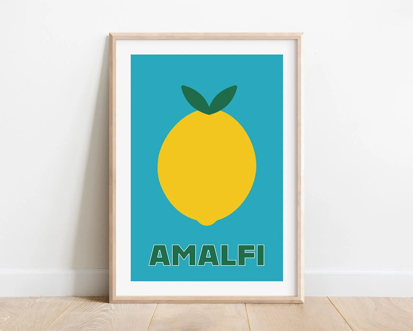 A vibrant yellow Amalfi lemon print on a bright blue background, styled inside a light oak wooden frame hanging on a clean white interior kitchen wall