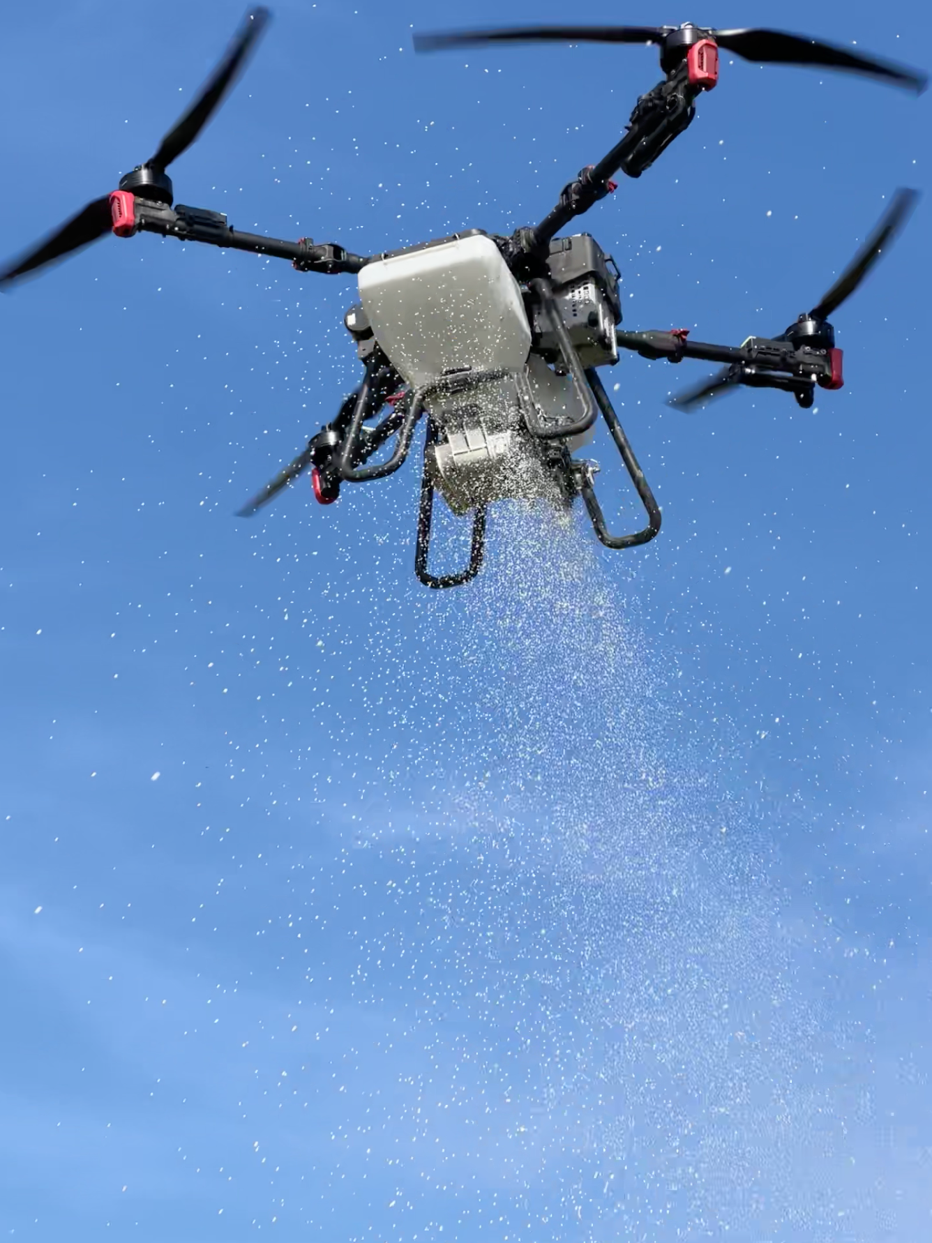 A drone flying in a clear blue sky with water droplets falling from it.