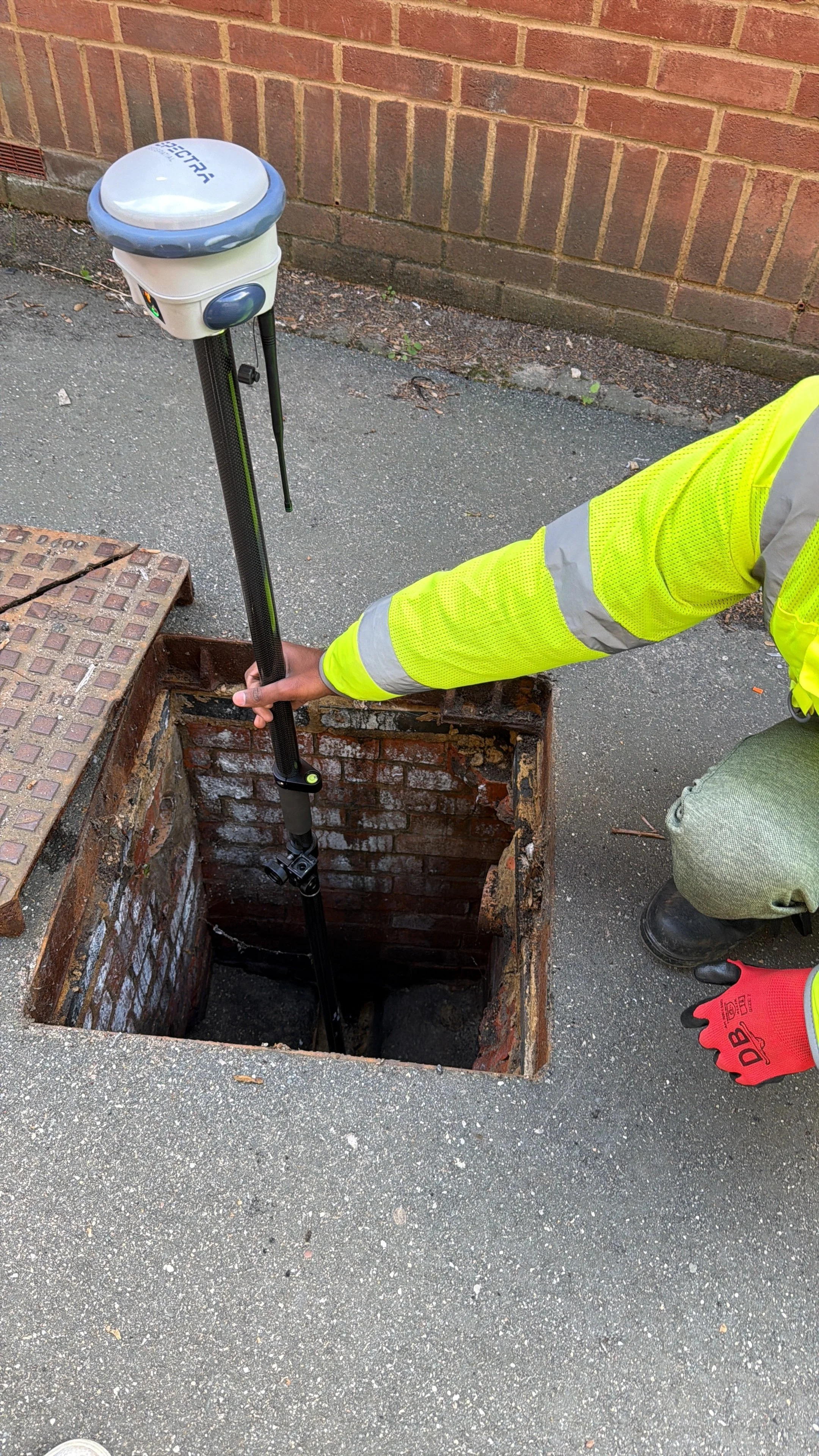 AKN Engineering site engineer in Hertfordshire using a Spectra GNSS GPS receiver to accurately survey and map underground utilities through an open manhole. High-precision underground utility survey for mapping and geolocation data collection.