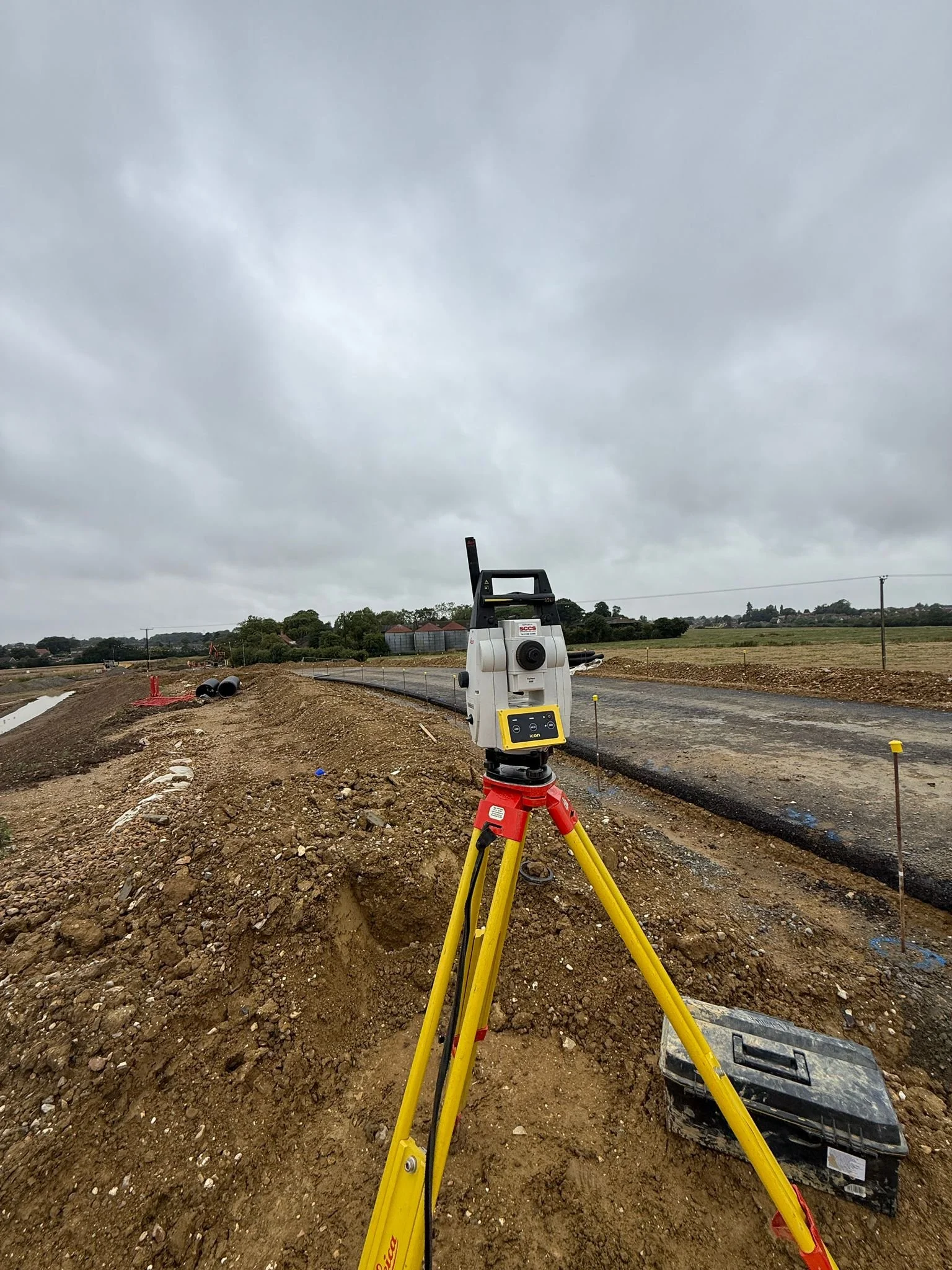 Surveying equipment on a construction site with a dirt road and cloudy sky