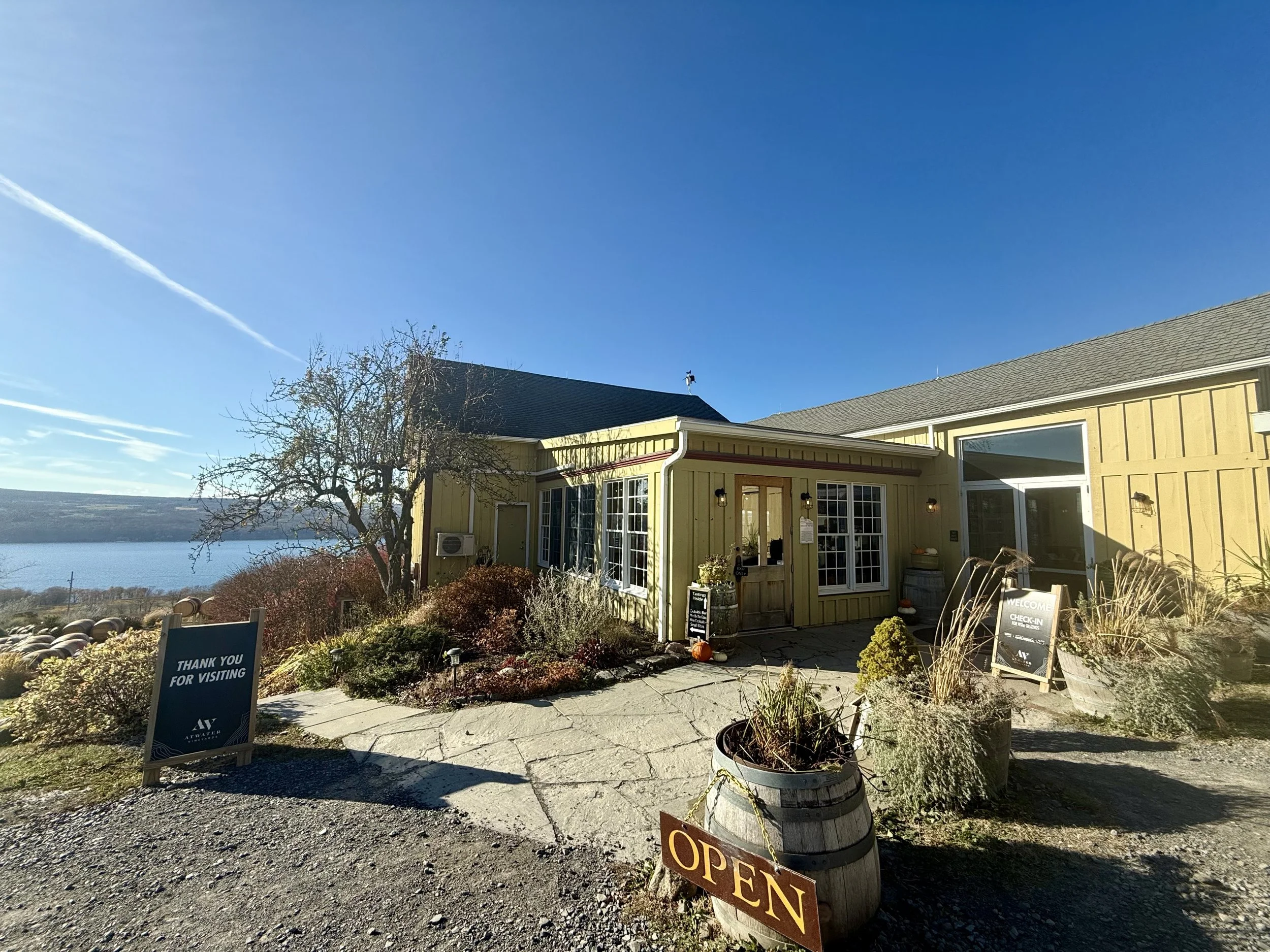 Yellow building with large windows and outdoor sign that says "OPEN," located next to a body of water and clear blue sky.