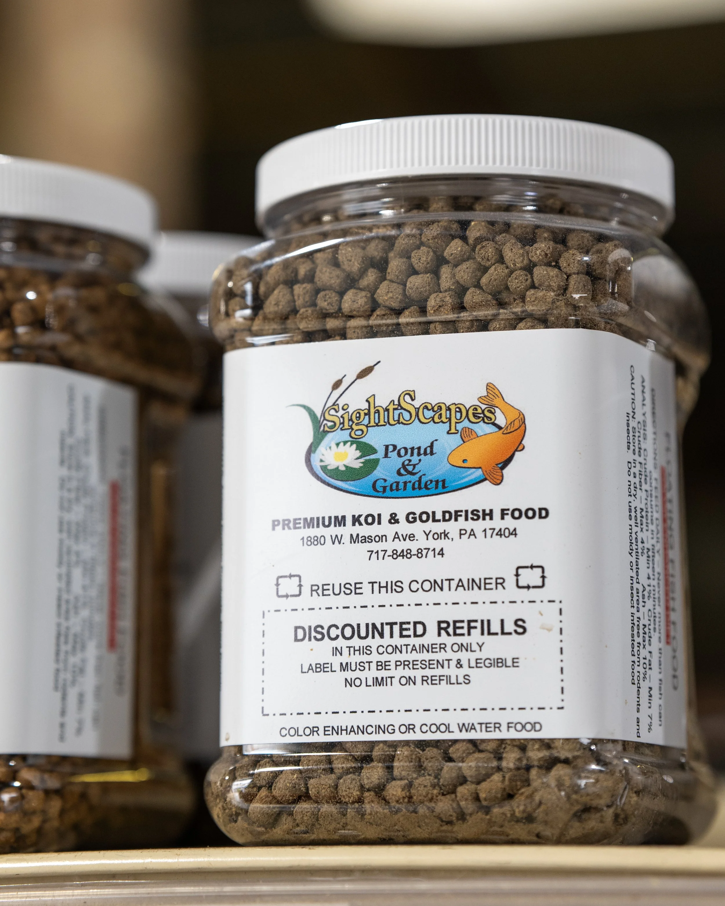 Container of fish food labeled 'SightScapes Pond & Garden, Premium Koi & Goldfish Food' with a picture of a fish, address in York, PA, and information on discounted refills.