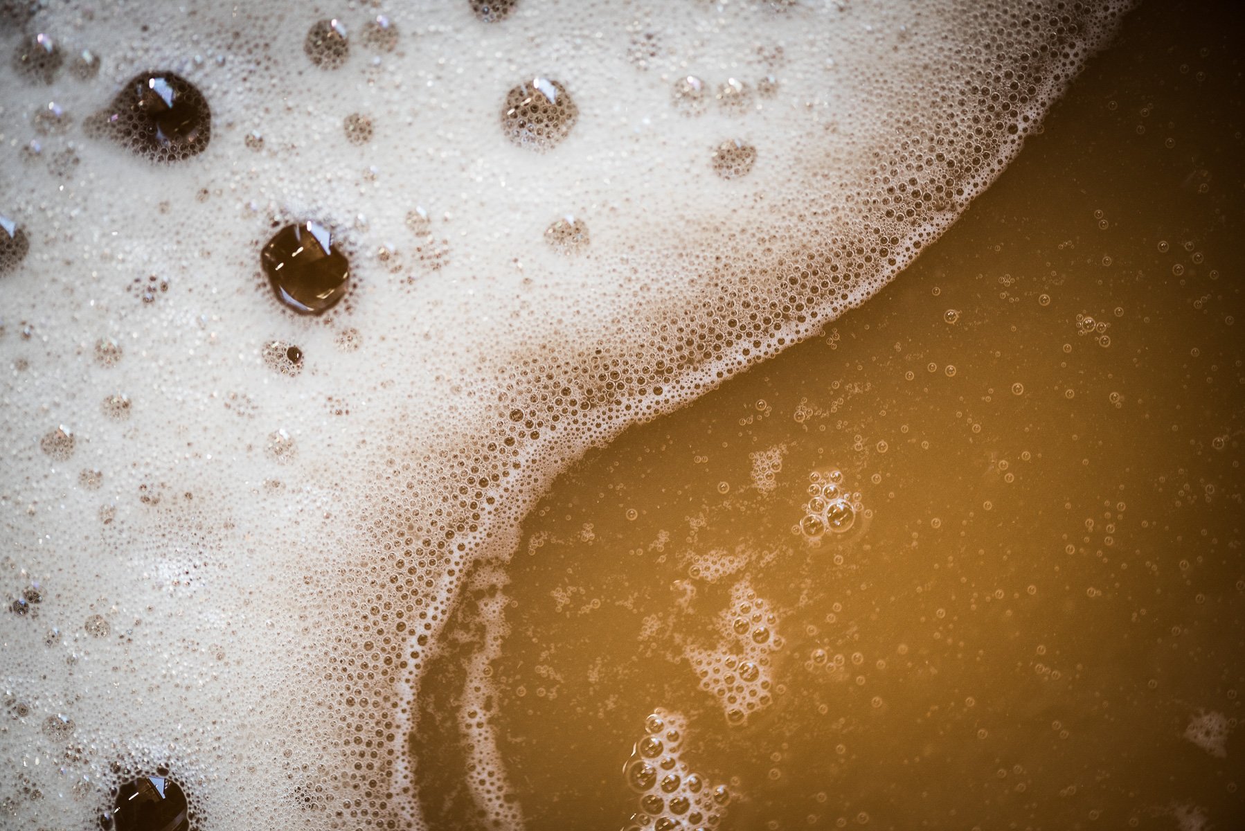 Gros plan de mousse de savon avec des bulles et du liquide brun, probablement du café ou du thé.
