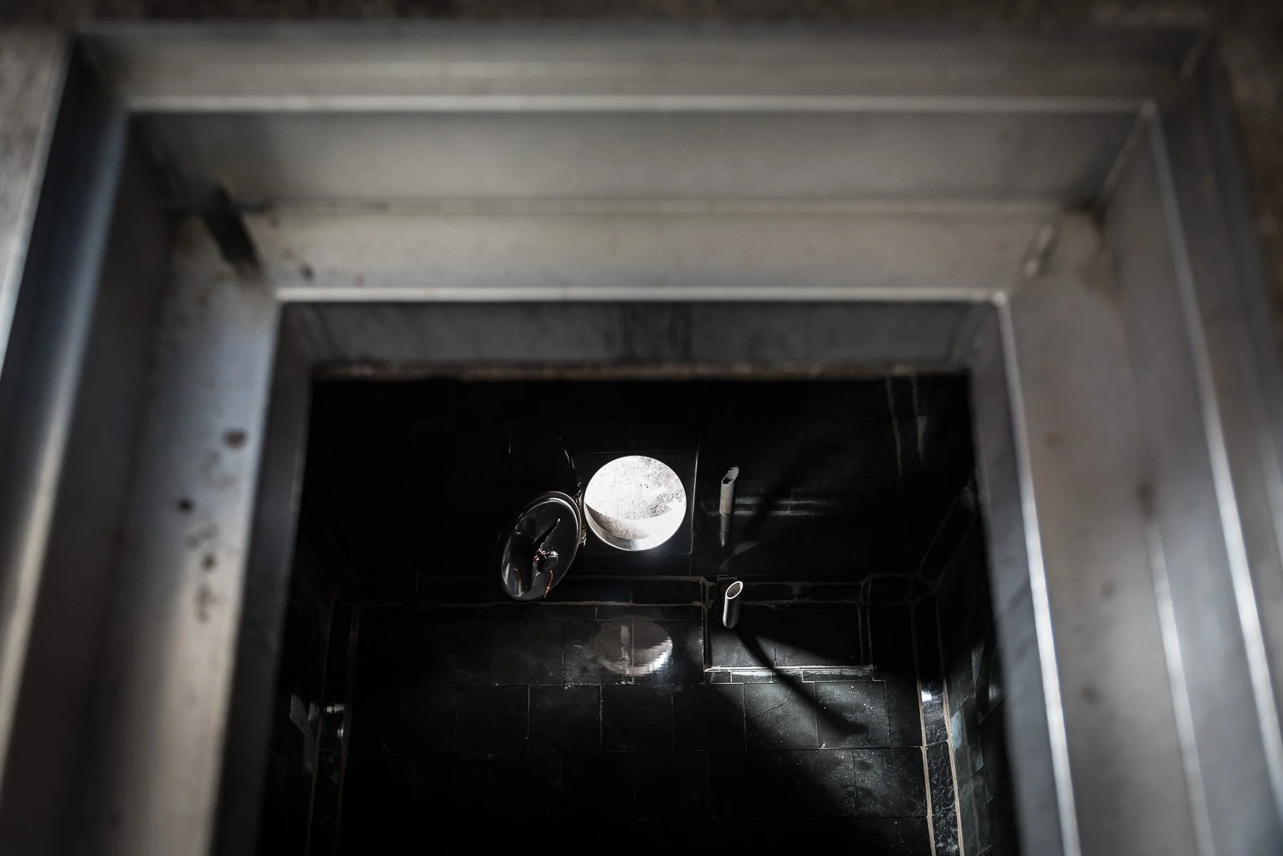 Vue du dessus d'un escalier en métal menant à un sol noir brillant avec une lampe ronde et deux tuyaux visibles.