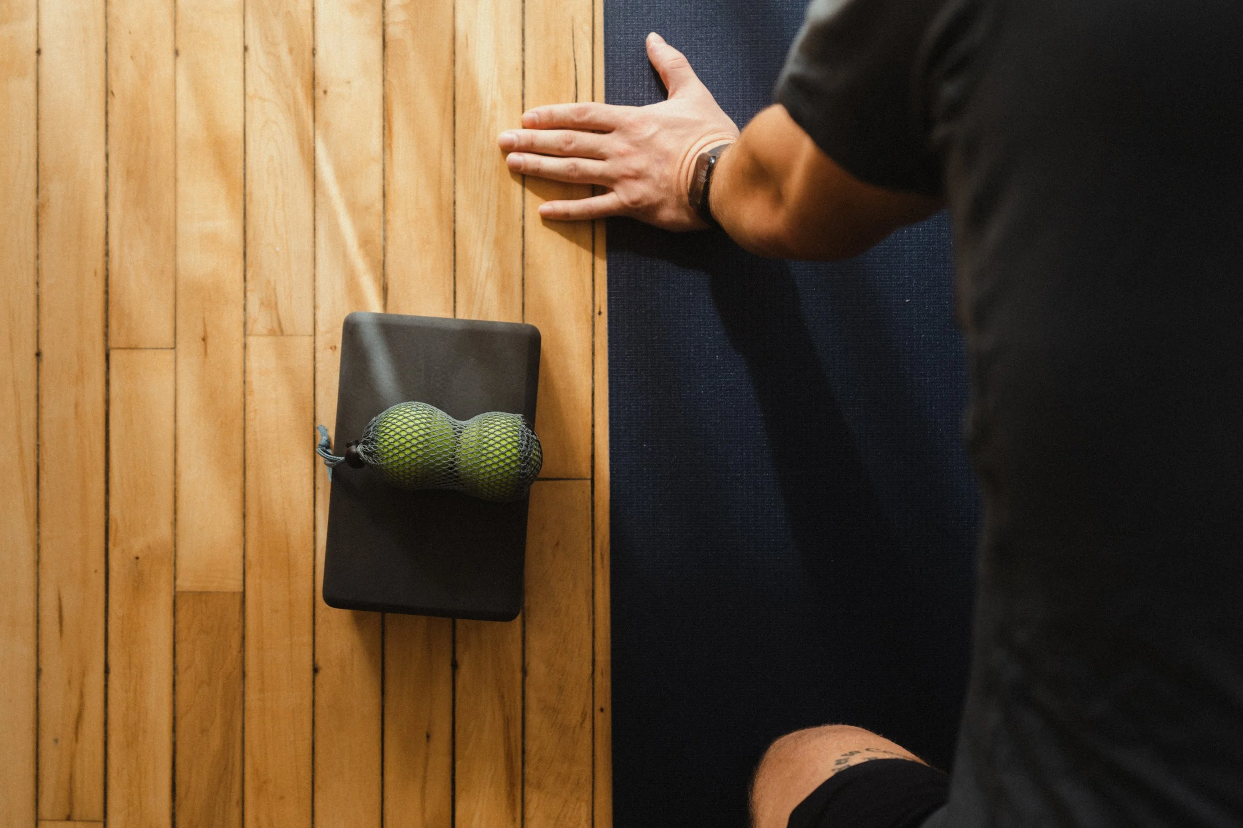 Person doing a wrist stretch on a yoga mat next to Yoga Tune Up balls.