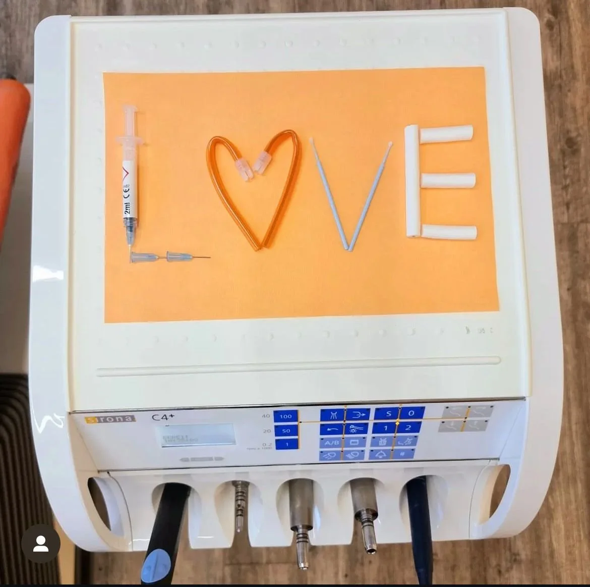 Das Wort 'LOVE' ist auf einem medizinischen Gerät mit einzelnen Buchstaben aus verschiedenen medizinischen Instrumenten gestaltet. Das 'L' ist aus einer Spritze, das 'O' ist ein Herz aus einem Schlauch, das 'V' ist ein Draht, und das 'E' besteht aus weißen medizinischen Röhren.