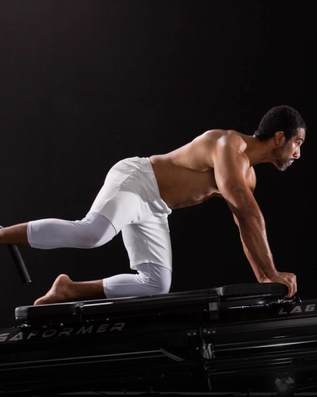 Man wearing white shorts on a silent treadmill, hiking in a plank position with one knee raised.