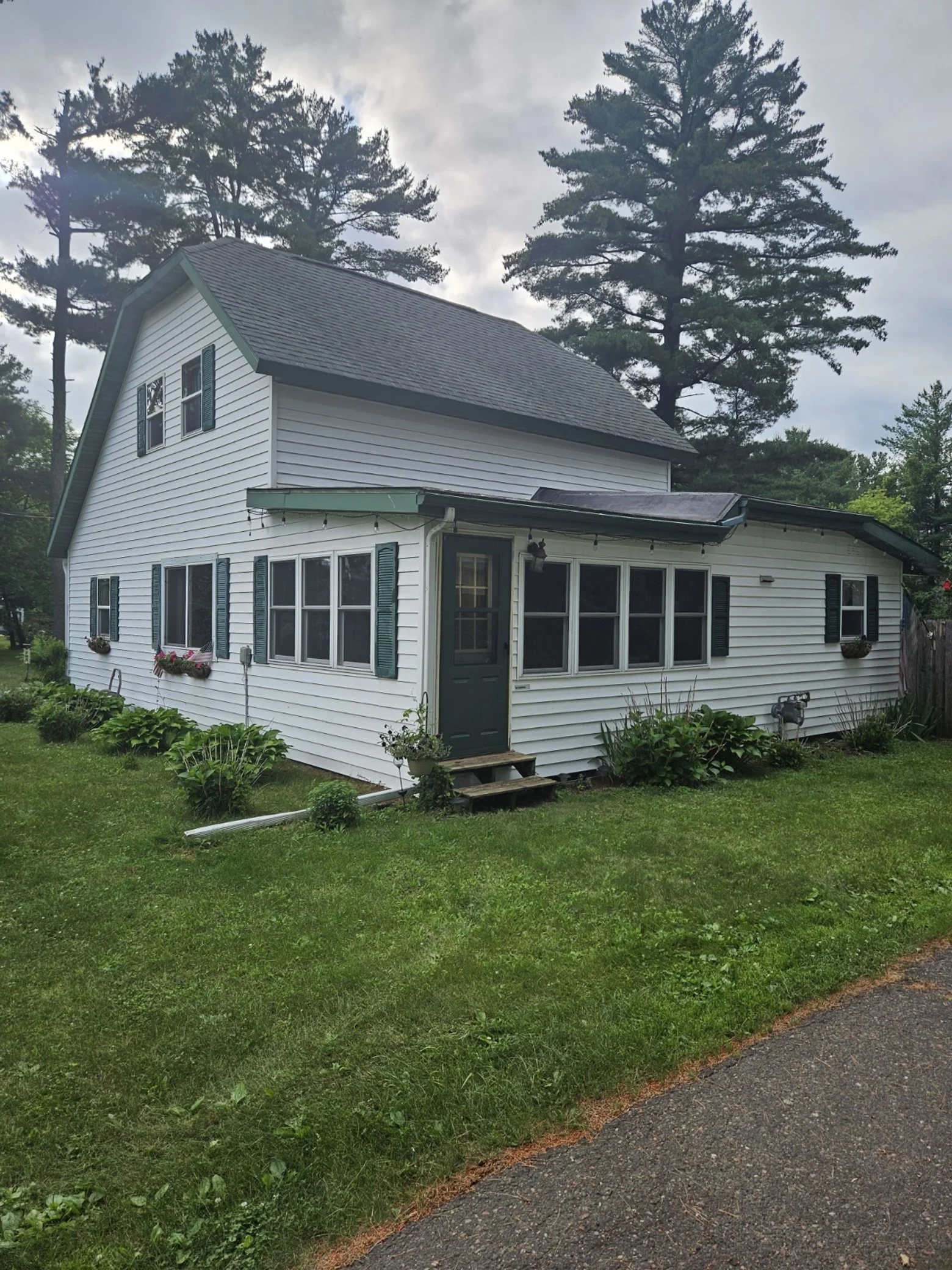 White two-story house with green shutters, green door, and hanging flower baskets, surrounded by green lawn and trees.