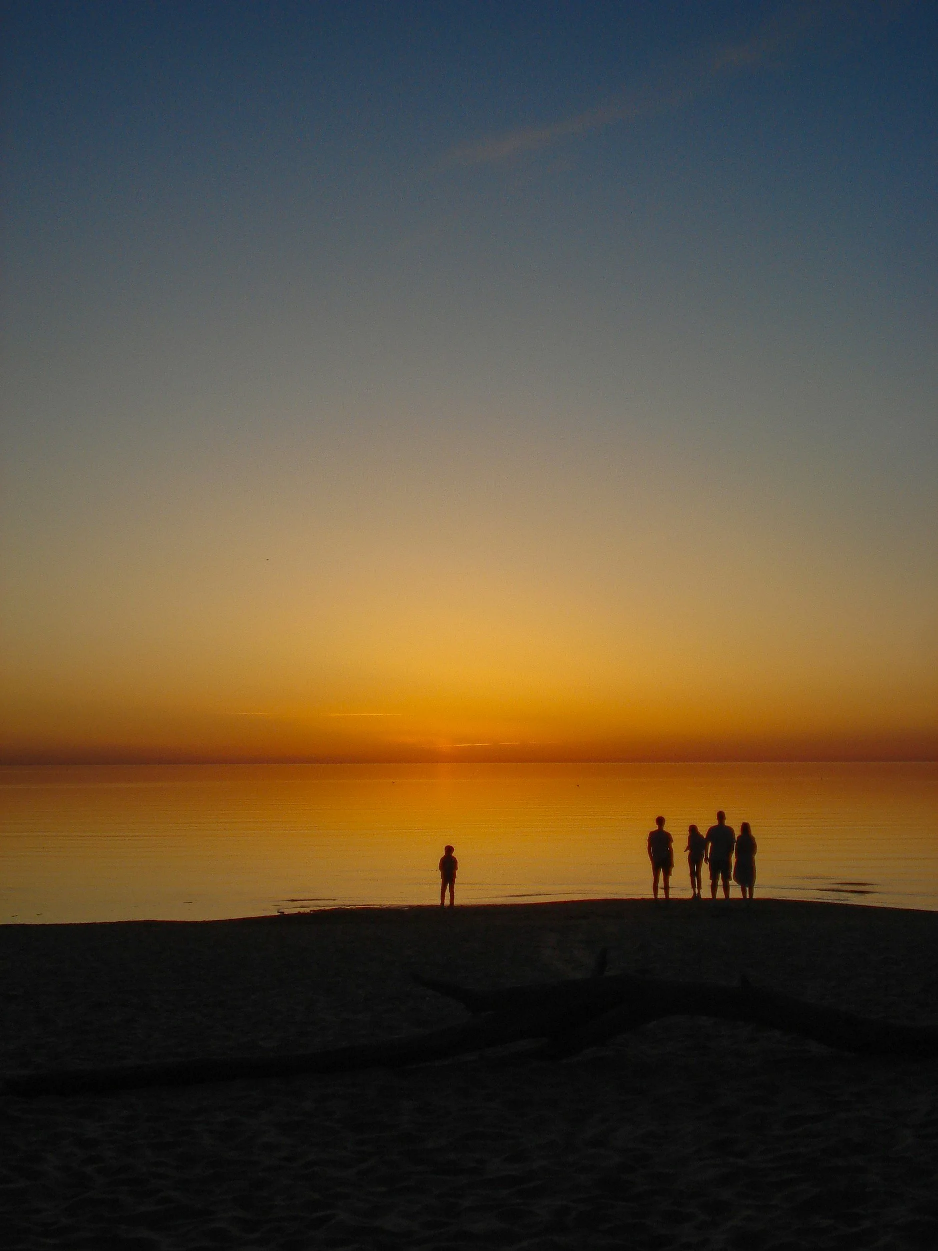 Silhouettes of a family walking on the beach during sunset with a colorful sky.
