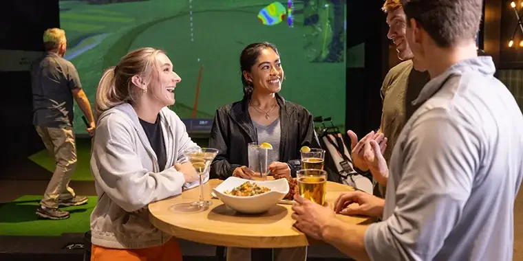People socialize in an indoor golf simulator space