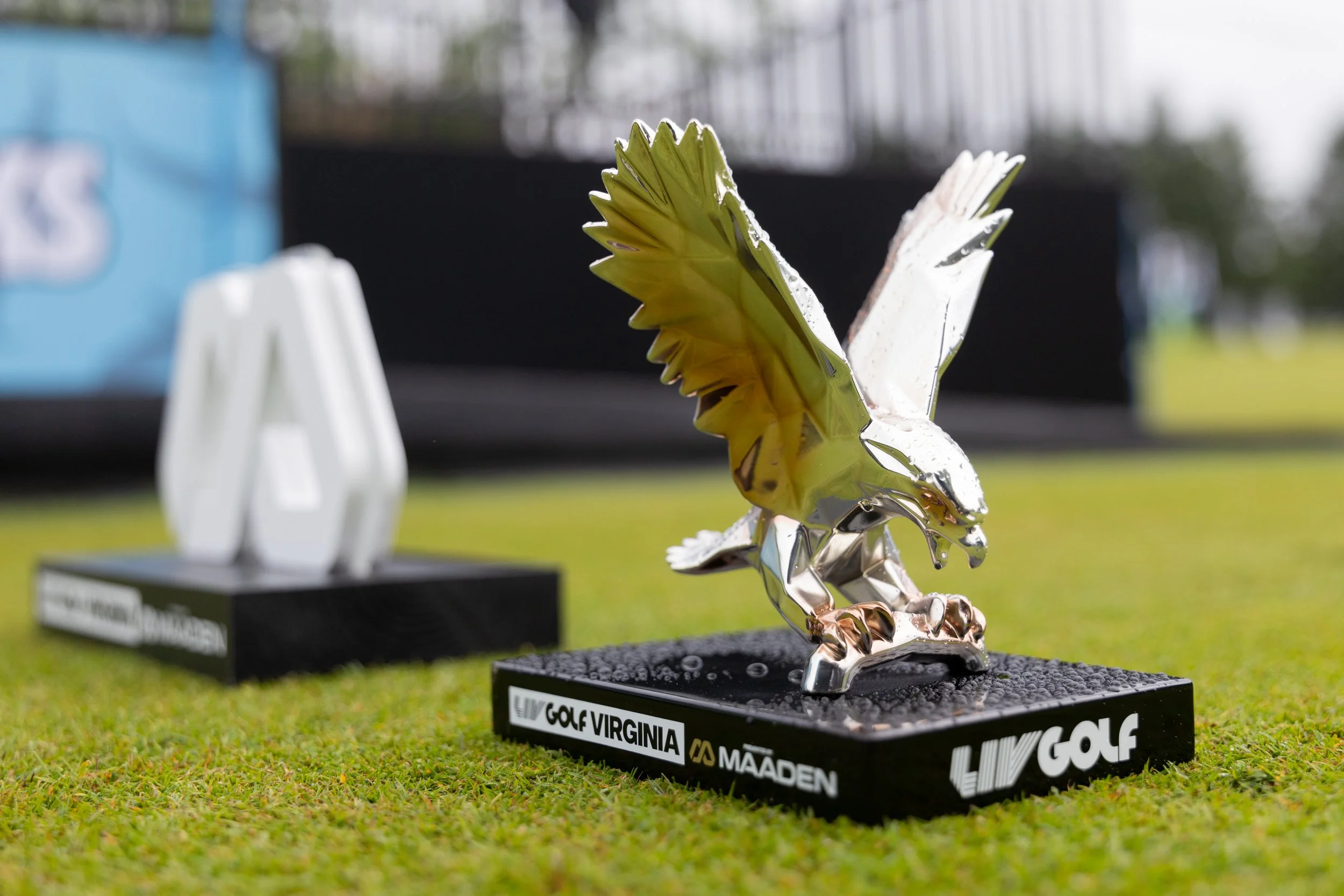 A metallic eagle trophy with yellow and silver accents on a black base, placed on a grassy field during a golf event.