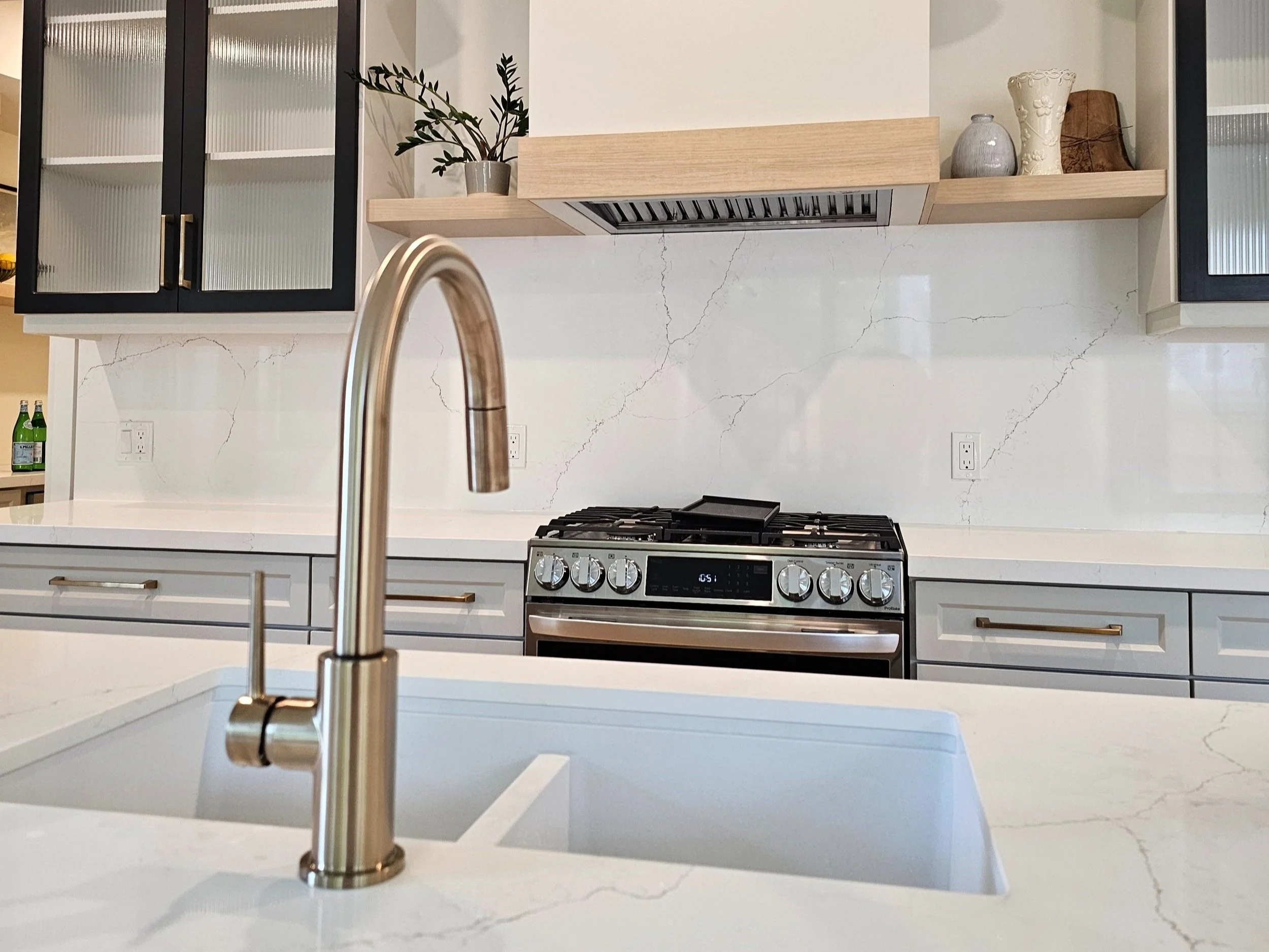 Modern kitchen with white marble countertop, stainless steel faucet, black and gray cabinetry, and a stainless steel gas stove with digital display.
