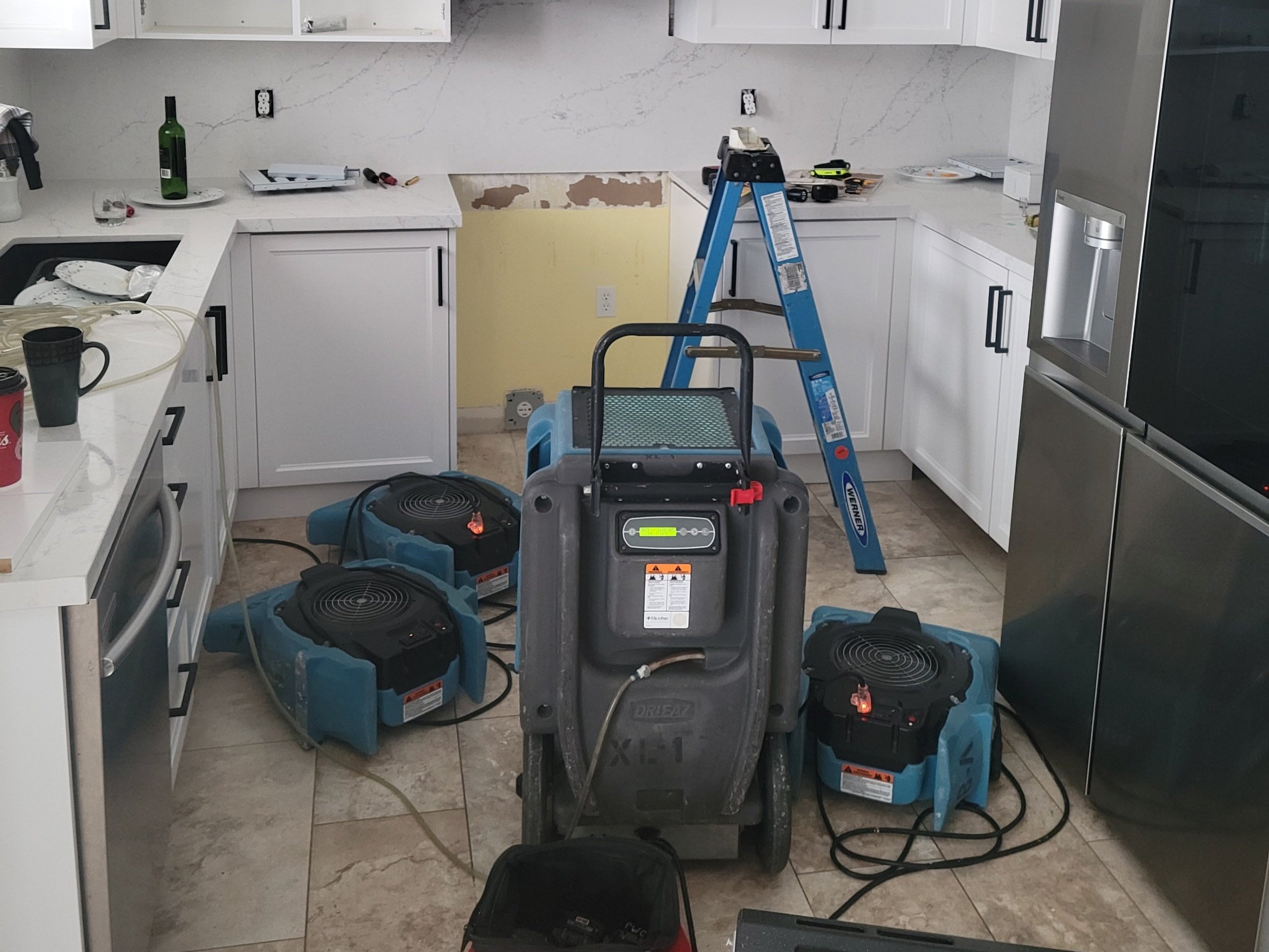 Kitchen under renovation with tools and equipment, including a ladder, duct cleaning machines, and construction supplies.
