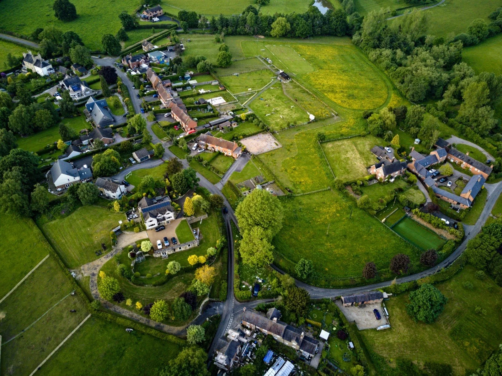 An aerial view of a residential community with houses, green lawns, and trees surrounded by open fields and farmland.
