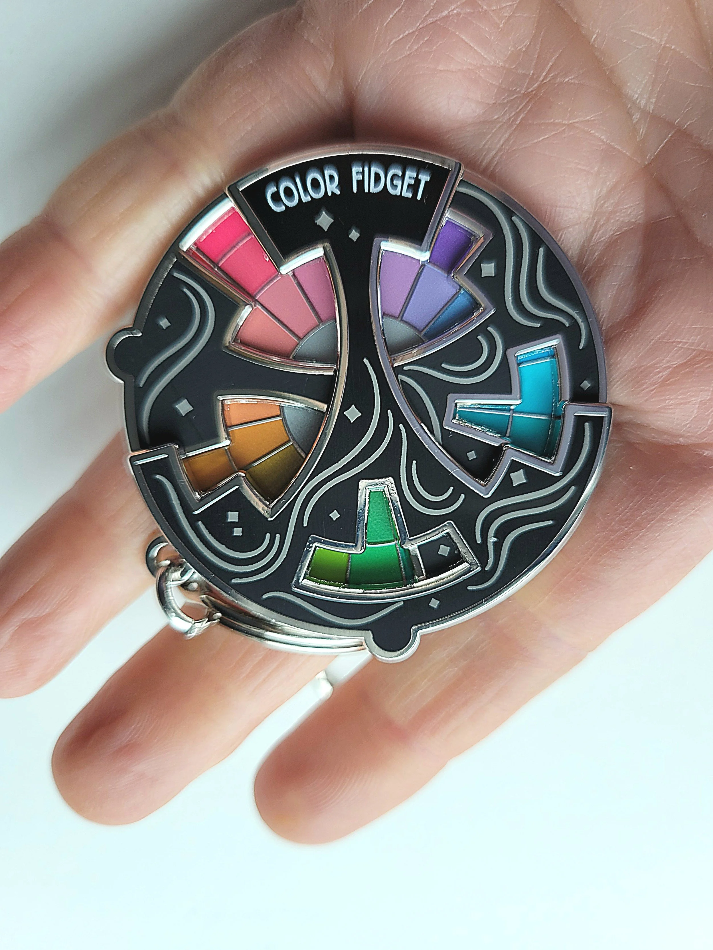 A person holding a round, multi-colored fidget spinner with sections labeled 'Color Fidget' in the inner ring.