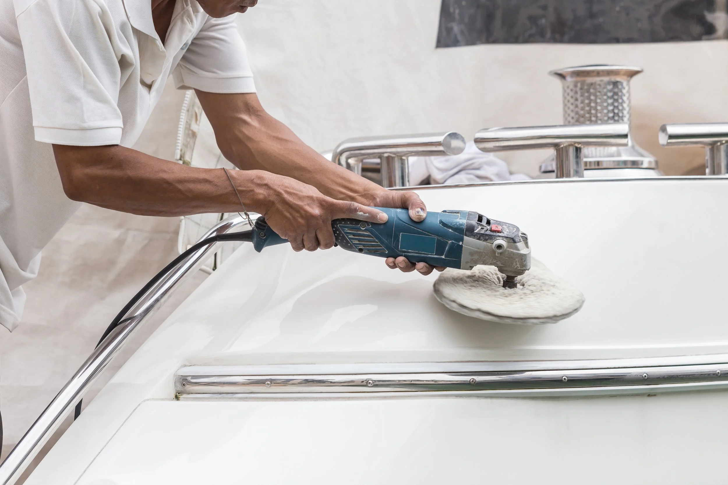 Person polishing a boat's surface with a power buffer.