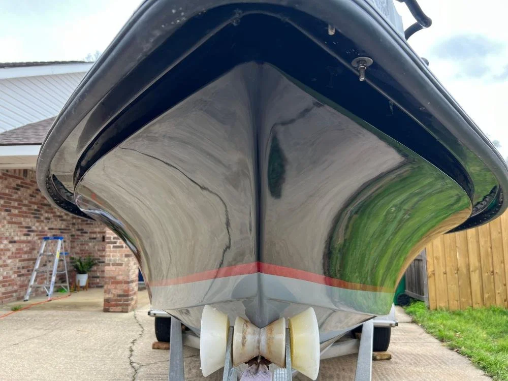 View of a boat's hull from the front, showing the keel and trailer, with part of a brick building and a ladder nearby.