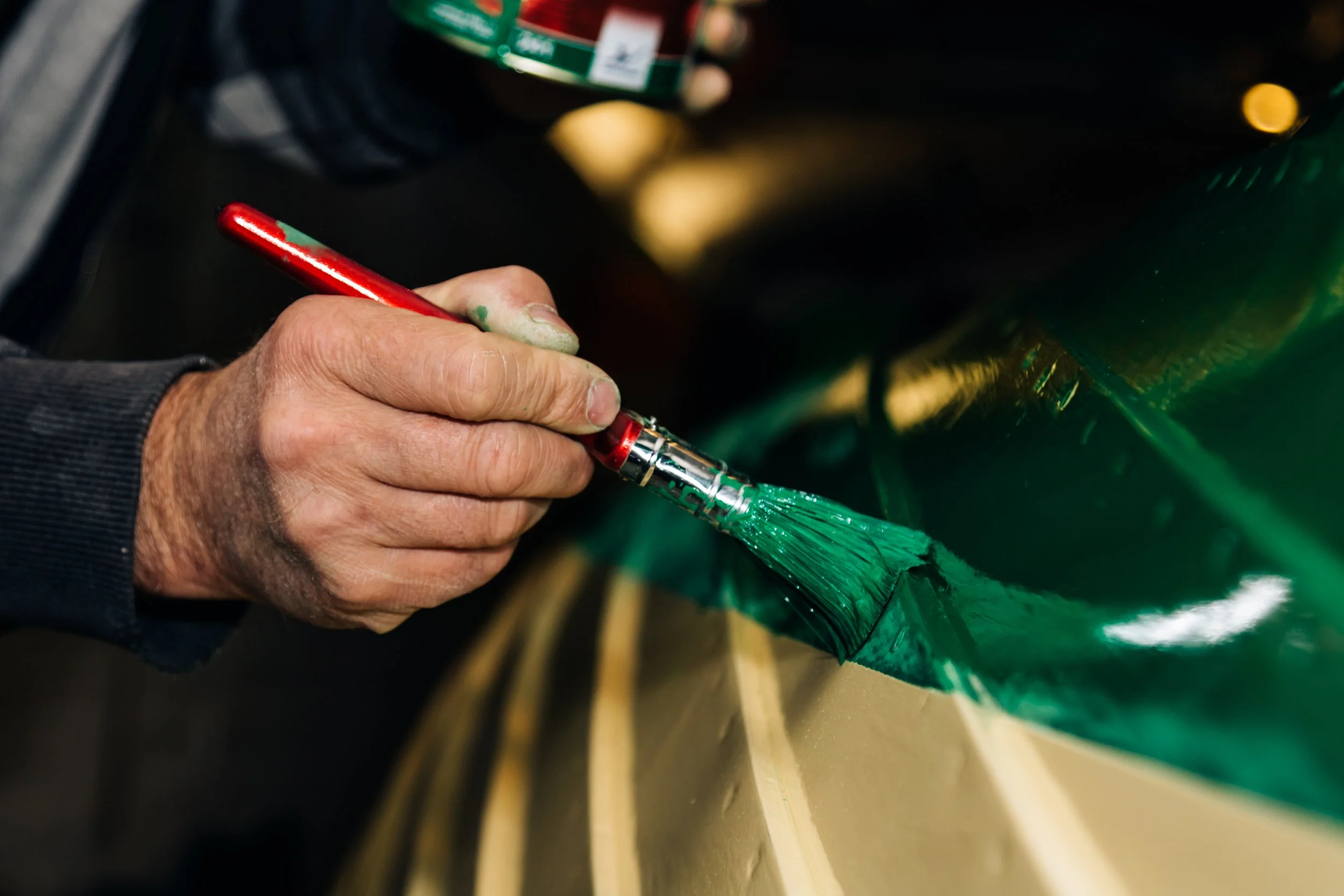 Close-up of a person painting a green stripe on an object with a small paintbrush.